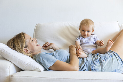 Glückliche Mutter auf der Couch liegend mit ihrem kleinen Mädchen, lizenzfreies Stockfoto