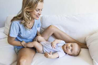 Happy mother playing with her baby girl on couch - TCF05875