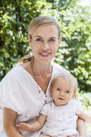 Portrait of smiling mother holding her baby girl outdoors stock photo