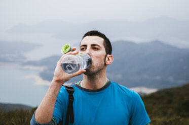 Männlicher Wanderer trinkt Wasser, während er auf einem Berg gegen den Himmel steht - CAVF49666