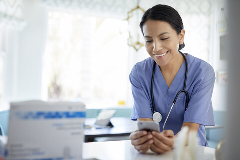 Lächelnde Ärztin, die bei der Arbeit im Krankenhaus ein Smartphone benutzt, lizenzfreies Stockfoto
