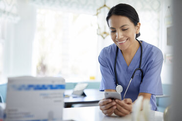 Lächelnde Ärztin, die bei der Arbeit im Krankenhaus ein Smartphone benutzt - CAVF49676
