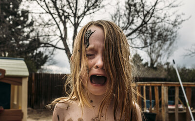 Close-up of girl crying and screaming with mud on face at backyard - CAVF49692