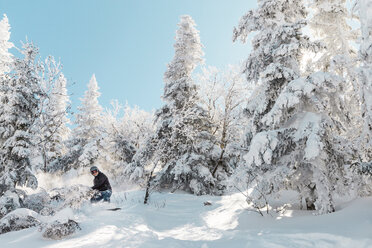 Mann beim Snowboarden auf Schnee gegen Bäume im Winter - CAVF49695