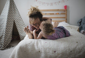 Tochter küsst glückliche Mutter, während sie zu Hause auf dem Bett liegt - CAVF49710