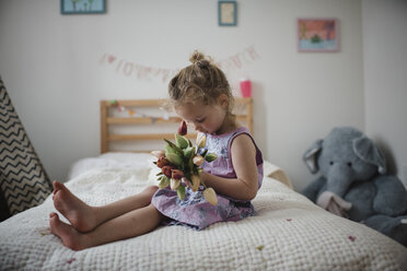 Girl holding tulips while sitting on bed at home - CAVF49714