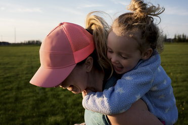 Close-up of happy mother piggybacking daughter while running at park against sky during sunset - CAVF49718