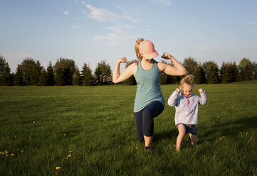 Mother with daughter exercising on grassy field at park against sky during sunset - CAVF49720