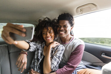 Glückliches Paar, das ein Selfie macht, während es im Auto unterwegs ist - CAVF49729