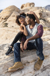 Happy couple sitting on rock formation - CAVF49733