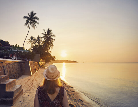 Rückansicht einer Frau mit Hut am Strand gegen den Himmel bei Sonnenuntergang, lizenzfreies Stockfoto