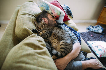 Hoher Blickwinkel auf einen Mann mit einer Katze, die auf dem Sofa zu Hause schläft - CAVF49748