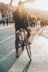 Männlicher Radfahrer, der beim Radfahren auf einer Brücke in der Stadt bei Sonnenuntergang wegschaut - CAVF49750