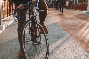 Low section of cyclist riding bicycle on bridge in city during sunset - CAVF49751