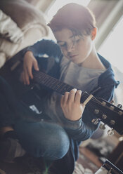 Boy playing guitar while sitting at home - CAVF49758