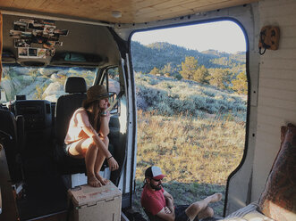 High angle view of couple looking at view while sitting in motor home at forest - CAVF49778