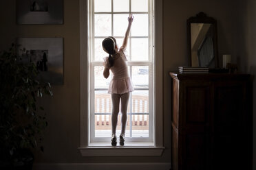 Rear view of girl in ballet costume closing window at home - CAVF49792