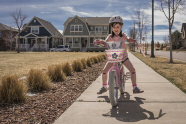 Happy girl riding bicycle on road against sky during sunny day - CAVF49795