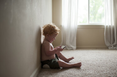 Seitenansicht des hemdlosen niedlichen Babyjungen, der ein Smartphone benutzt, während er auf dem Teppich zu Hause sitzt - CAVF49797