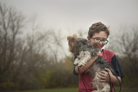 Glücklicher Junge mit Hund im Park gegen den klaren Himmel stehend, lizenzfreies Stockfoto