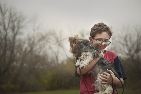 Glücklicher Junge mit Hund im Park gegen den klaren Himmel stehend - CAVF49804