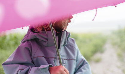 Midsection of girl carrying umbrella while standing outdoors during rainy season - CAVF49813