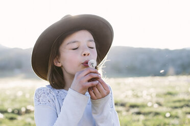 Close-up of girl with eyes closed blowing dandelion seed while standing against sky during sunny day - CAVF49826