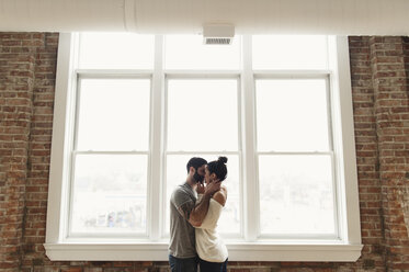 Romantic couple kissing while standing by window at home - CAVF49832