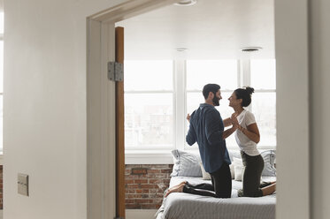 Romantisches Paar hält sich an den Händen, während es auf dem Bett kniet, gesehen durch die Türöffnung zu Hause - CAVF49837