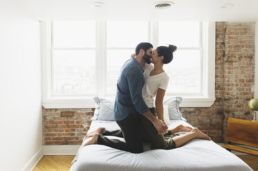 Romantisches Paar küsst sich auf dem Bett kniend zu Hause - CAVF49838