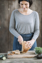 Frau schneidet Brot auf einem Holztisch zu Hause - CAVF49847