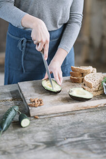 Midsection von Frau Schneiden Avocado auf Holztisch zu Hause - CAVF49848