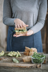 Mittelteil einer Frau, die ein Sandwich auf einem Holztisch zu Hause zubereitet - CAVF49852