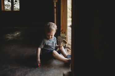 Baby boy with brush sitting at entrance in abandoned room - CAVF49864