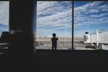 Rückansicht einer Silhouette eines kleinen Jungen, der durch ein Fenster im Abflugbereich eines Flughafens schaut - CAVF49866