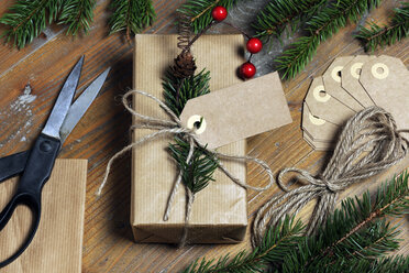 High angle view of Christmas present with labels and strings by pine needles on wooden table - CAVF49873