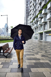 Junger Geschäftsmann mit Regenschirm in voller Länge auf dem Fußweg in der Stadt bei Regen - CAVF49895