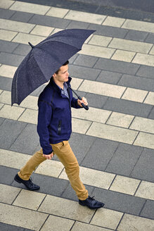 Hohe Winkel Ansicht der jungen Geschäftsmann mit Regenschirm zu Fuß auf dem Bürgersteig in der Stadt während des Regens - CAVF49897