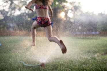 Niedriger Ausschnitt eines Mädchens in Badekleidung, das auf einem grasbewachsenen Feld im Hof läuft - CAVF49905