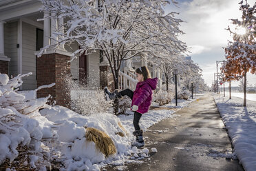 Seitenansicht des spielerischen Mädchen Tritte Schnee auf der Straße gegen bewölkten Himmel - CAVF49926