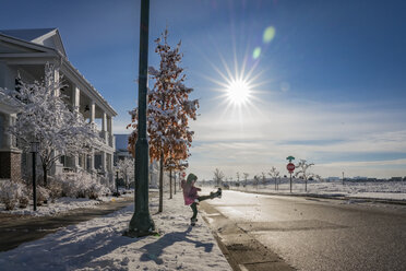 Seitenansicht des spielerischen Mädchen Tritte Schnee auf der Straße gegen den blauen Himmel während des sonnigen Tages - CAVF49928