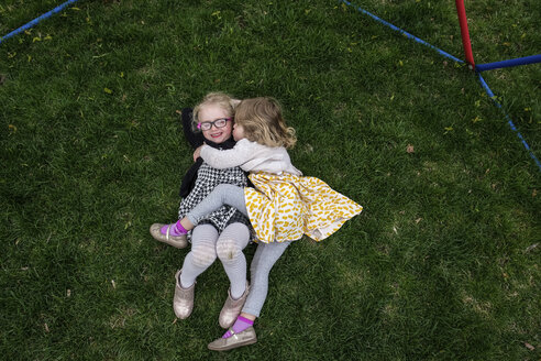 High angle view of happy sisters lying on grassy field at yard - CAVF49954
