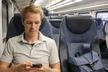 Mann benutzt Smartphone im Zug sitzend - CAVF49955