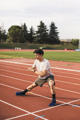 Athlete sitting doing warm-up exercises on a tartan track - ACPF00347