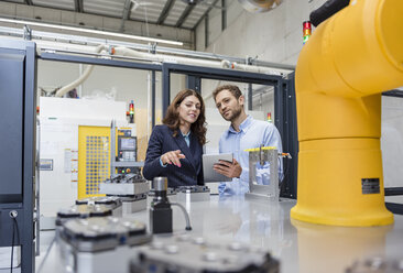 Colleagues in high tech company controlling industrial robots, using digital tablet - DIGF05145