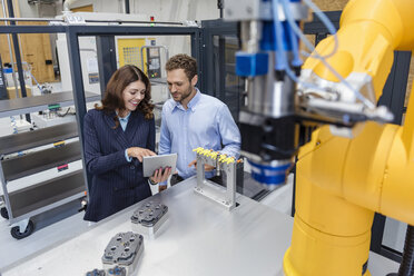 Colleagues in high tech company controlling industrial robots, using digital tablet - DIGF05146
