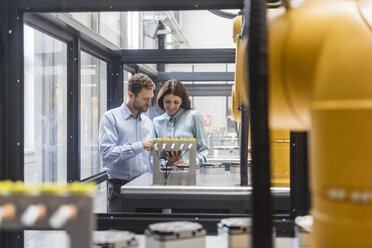 Colleagues in high tech company controlling industrial robots, using digital tablet - DIGF05158