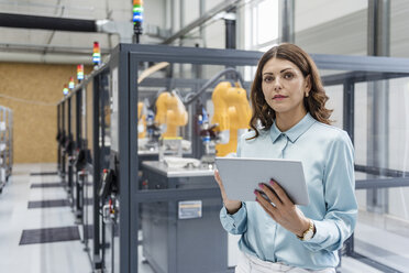 Businesswoman in high tech company controlling industrial robots, using digital tablet - DIGF05163