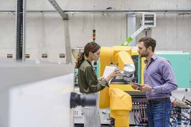 Geschäftsmann und Frau bei einer Besprechung vor Industrierobotern in einem Hightech-Unternehmen - DIGF05226