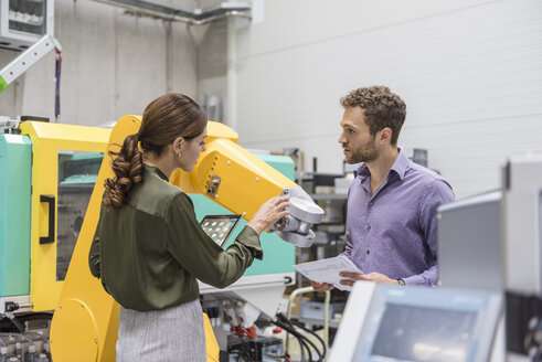 Geschäftsmann und Frau bei einer Besprechung vor Industrierobotern in einem Hightech-Unternehmen - DIGF05227